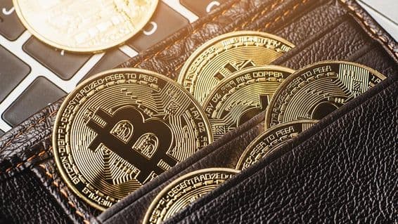 Moneda de Bitcoin en una billetera de cuero sobre un teclado de computadora.