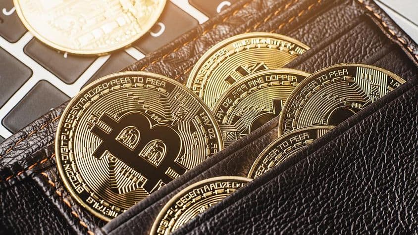 Moneda de Bitcoin en una billetera de cuero sobre un teclado de computadora.