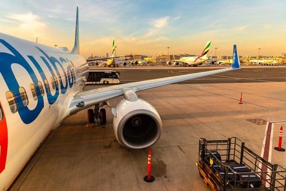 Avión de flydubai estacionado con varios otros aviones al fondo y un autobús de transporte de pasajeros, a la derecha con equipaje en un pequeño vehículo de transporte.