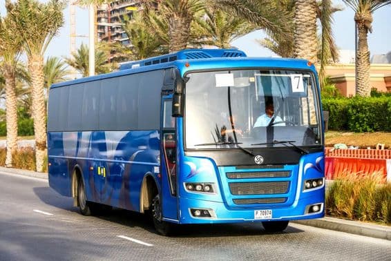 Autobús azul de Dubái con palmeras de fondo.