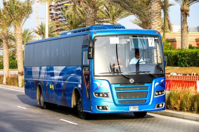 Autobús azul de Dubái con palmeras de fondo.
