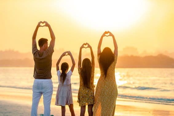 Gente en la playa de espaldas a la cámara, formando un corazón con las manos, con el mar de fondo.