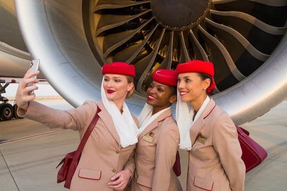 Tres asistentes de vuelo de Emirates tomándose una selfie frente al motor de un avión de Emirates.