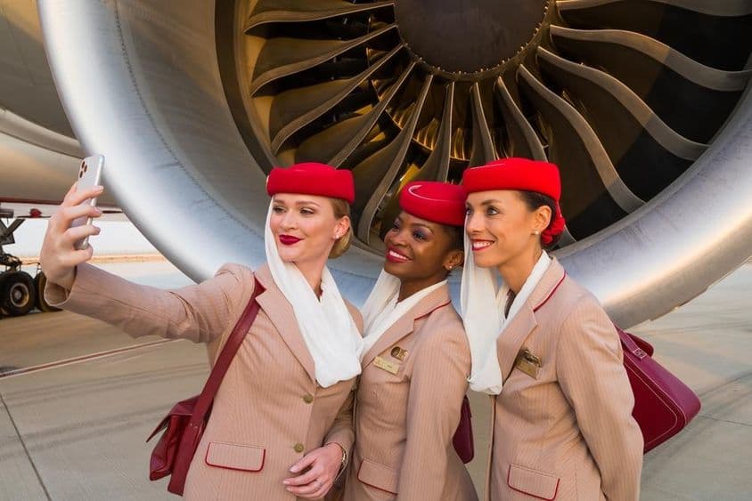 Tres asistentes de vuelo de Emirates tomándose una selfie frente al motor de un avión de Emirates.