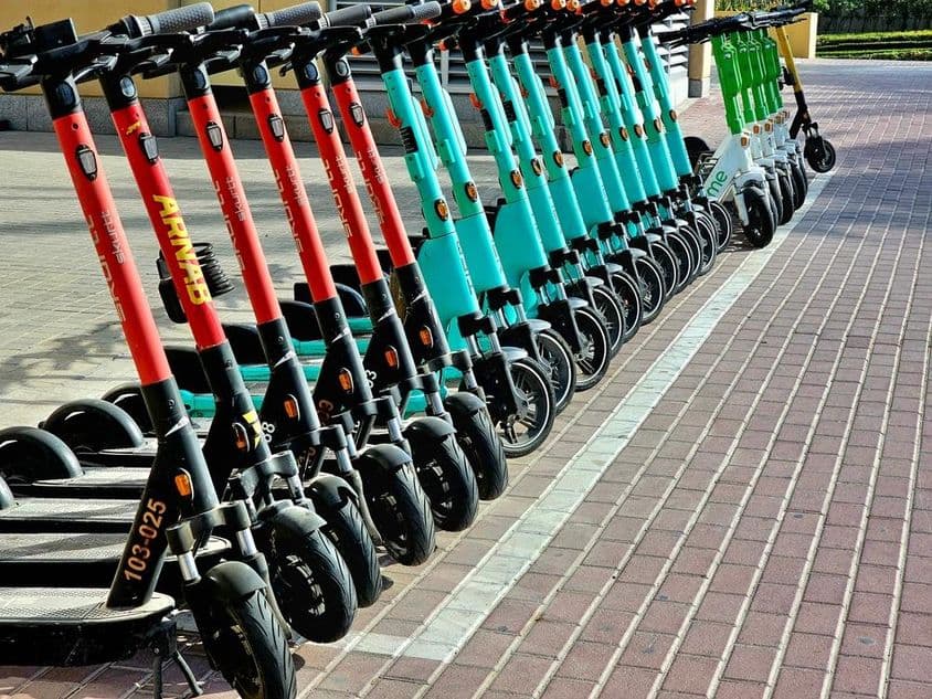 Scooters rojos, azules y verdes esperando en sus áreas de estacionamiento.