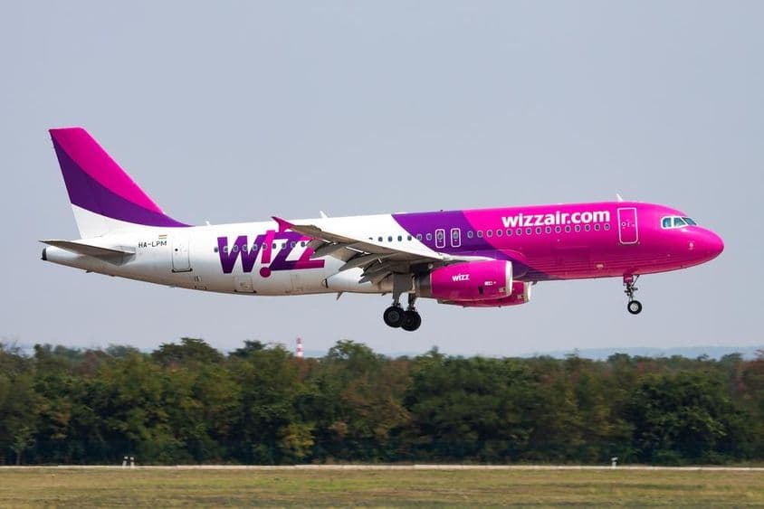 Avión de Wizz Air volando a baja altitud con bosque de fondo.