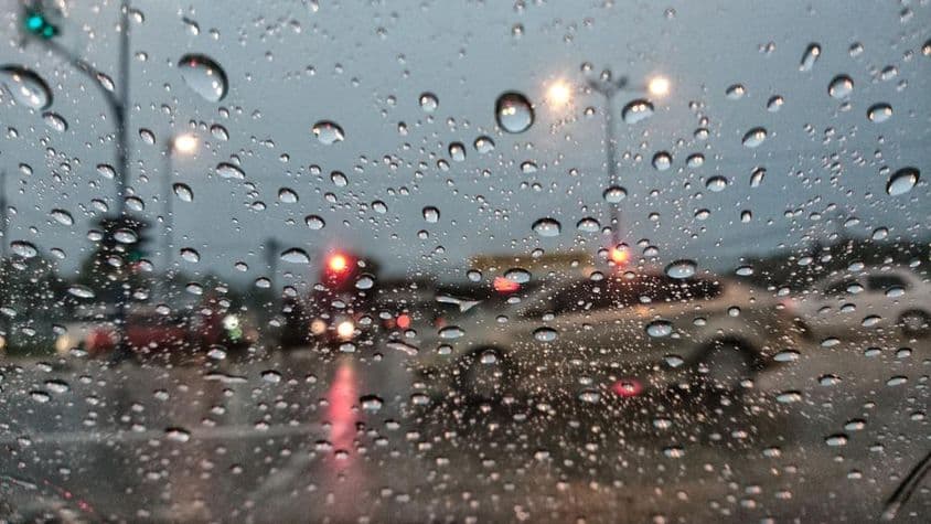 Coches apareciendo borrosos a través de un cristal cubierto de lluvia.
