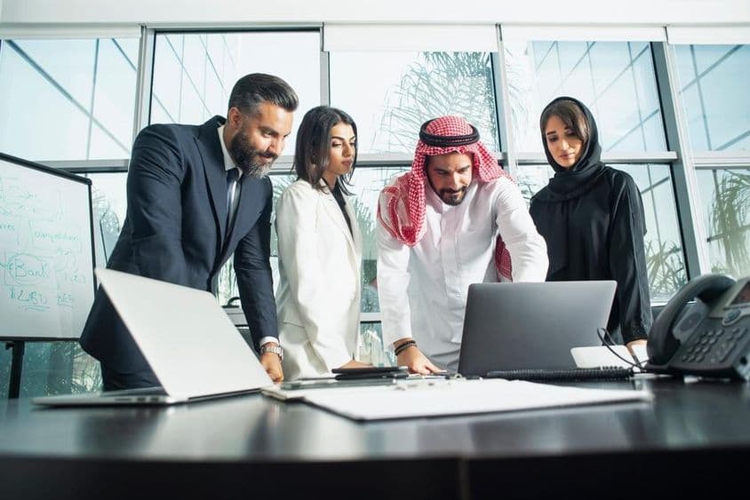 Ejecutivos de empresa deliberando en una oficina con laptop y teléfono enfrente.