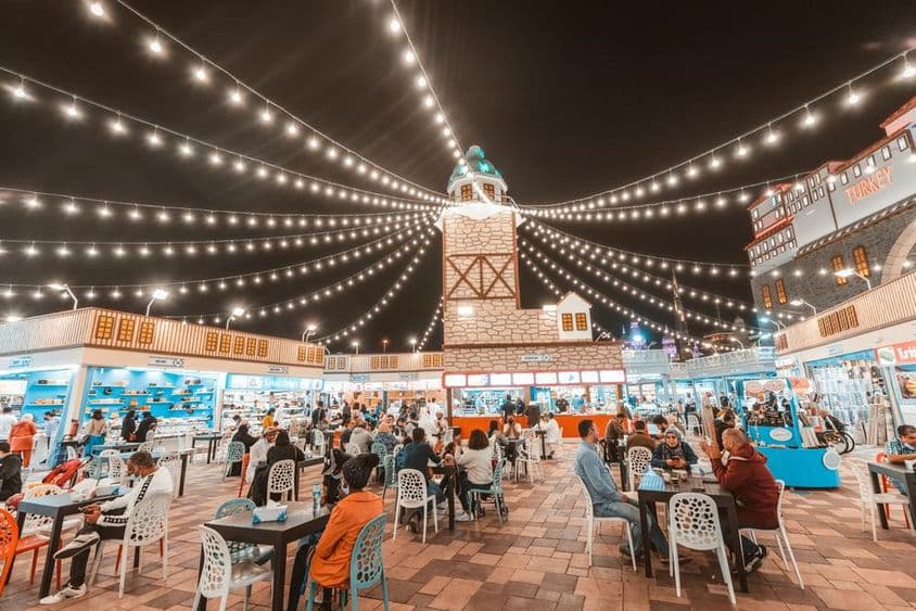 Global Village, turistas y locales probando especialidades culinarias en mesas.
