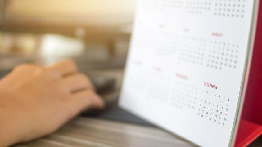 Una mano junto a un calendario, con meses borrosos, diciembre claramente visible.