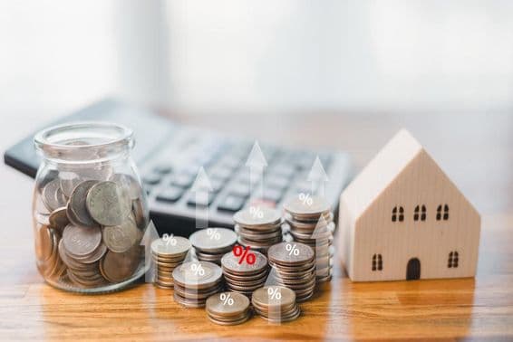 Monedas en un tarro de vidrio, monedas amontonadas junto a él, con un teclado al fondo, y un edificio de madera al lado.