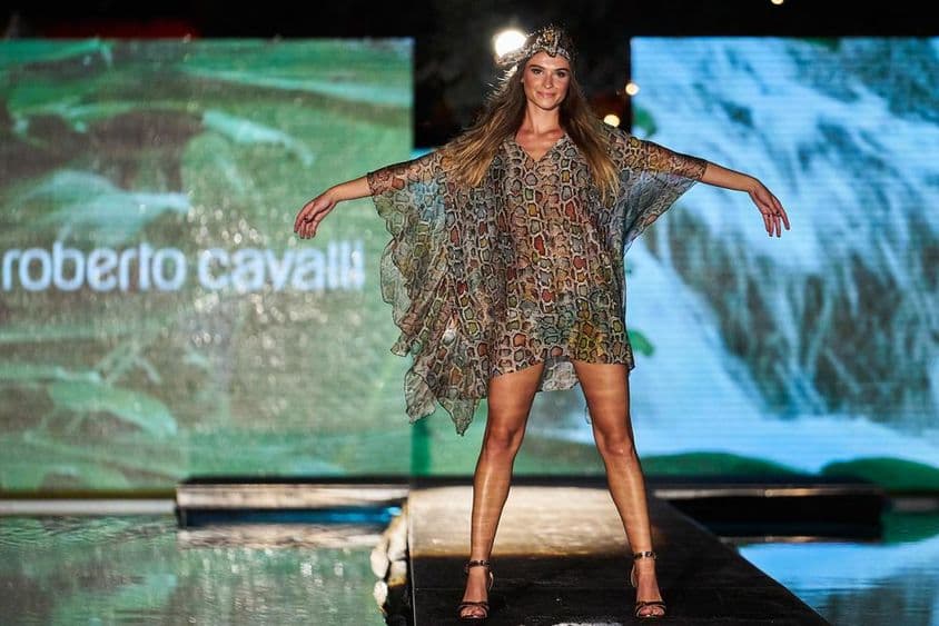 Cartel de Roberto Cavalli exhibido en el fondo, delante figura femenina en vestido de Roberto Cavalli en la pasarela.