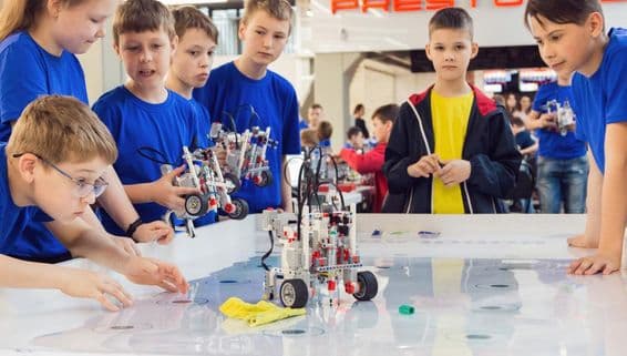Estudiantes con camisetas azules construyendo y programando un robot.