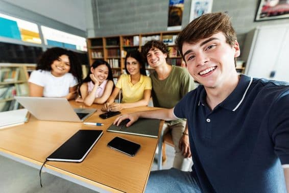 Estudiantes estudiando en la biblioteca con un portátil, teléfono y bloc de notas sobre el escritorio.