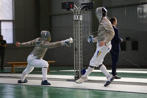 Dos esgrimistas compitiendo en la pista, uno logrando un toque.