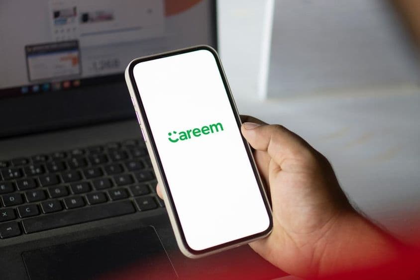 Una mano sostiene un teléfono con la aplicación Careem abierta, con un cuaderno visible en el fondo.