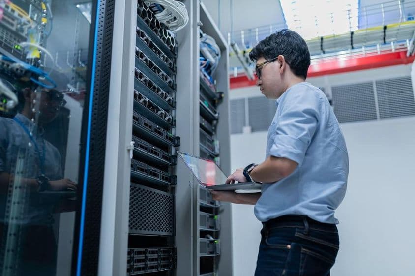 Una sala de servidores con una persona ajustando configuraciones en un portátil.