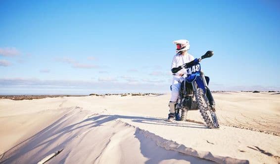 Persona andando en moto en el desierto, vistiendo ropa blanca sobre una motocicleta azul.
