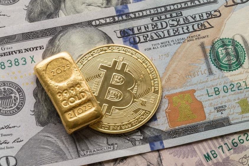 Una barra de oro de inversión y una moneda de Bitcoin sobre un billete de 100 dólares.