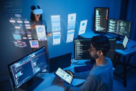 Un desarrollador de aplicaciones sentado frente a una computadora, sosteniendo una tableta, con dos monitores mostrando código de computadora.