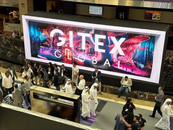 Gitex Global en el fondo con personas, principalmente hombres y mujeres emiratíes en primer plano.