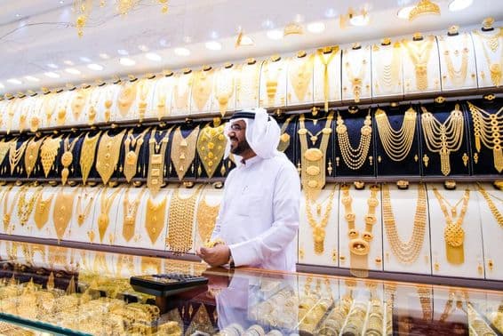 Vendedor de oro en Dubai, con un fondo de muchos collares de oro, el vendedor en atuendo tradicional blanco.