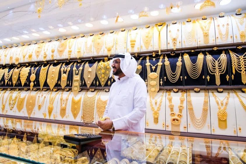 Vendedor de oro en Dubai, con un fondo de muchos collares de oro, el vendedor en atuendo tradicional blanco.