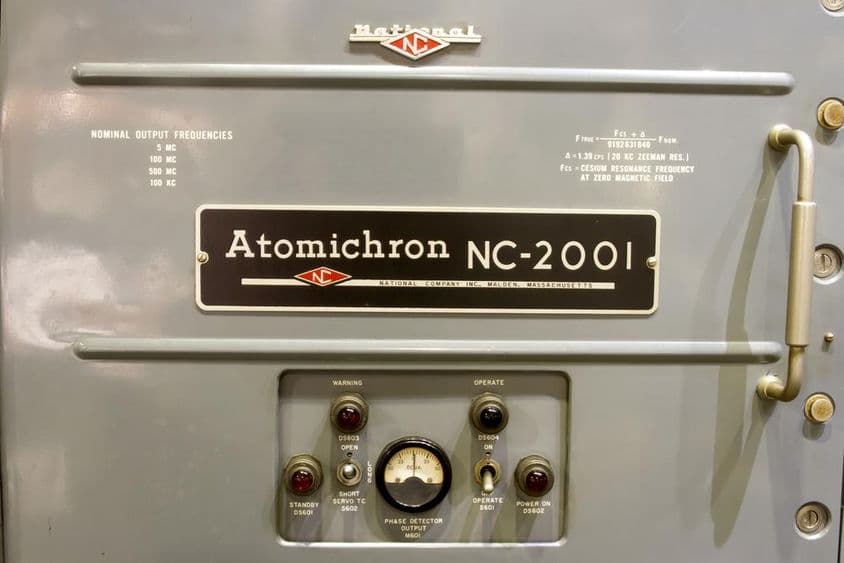 Se muestra el panel de control de un antiguo reloj atómico, junto con su nombre en una pequeña placa.