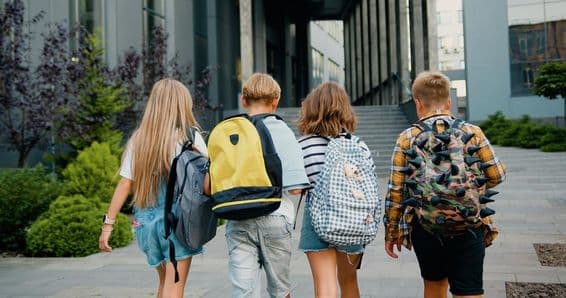 Estudiantes cargando mochilas frente a la entrada de una escuela.