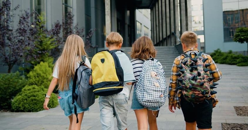 Estudiantes cargando mochilas frente a la entrada de una escuela.