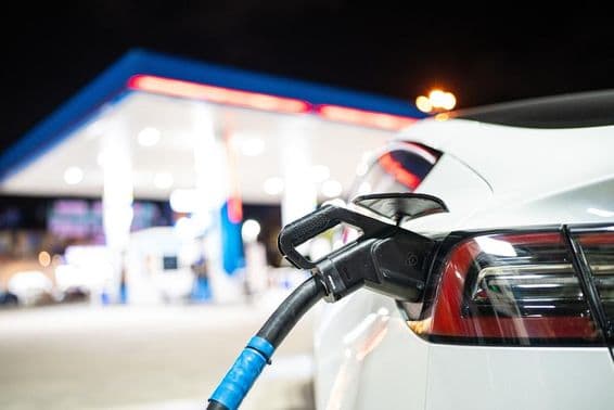 Un Tesla siendo cargado, con una gasolinera al fondo.