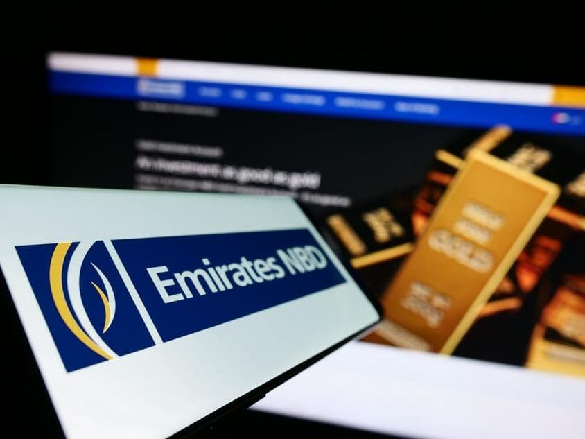Letrero de Emirates NBD en primer plano, fondo mostrando un lingote de oro de inversión.