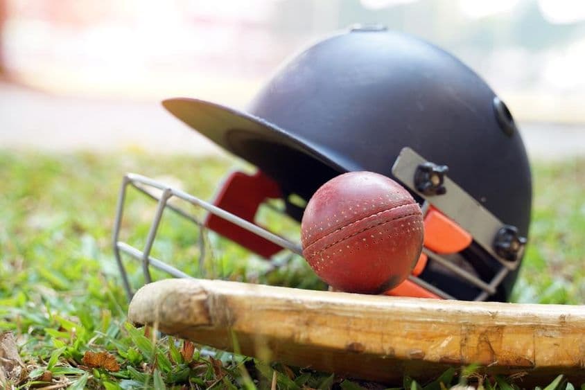 Un bate de cricket con una bola encima y detrás de él, un casco de cricket es visible en un campo de césped.