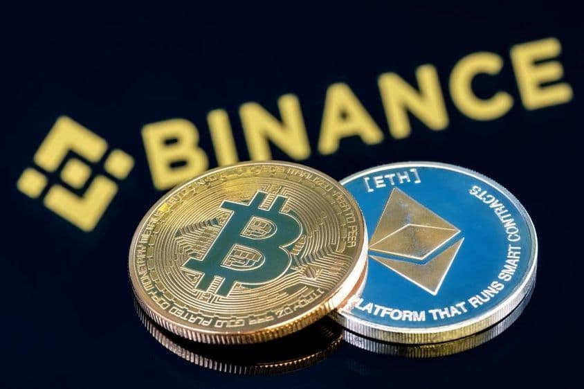 Inscripción de Binance en el fondo sobre una mesa negra con una moneda de Bitcoin y una de Ethereum.