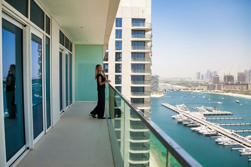 Una mujer en una terraza de Dubái observando barcos en el canal con un rascacielos de fondo.