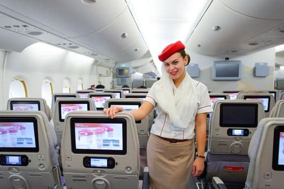 Interior de un avión de Emirates con un asistente de vuelo en primer plano.