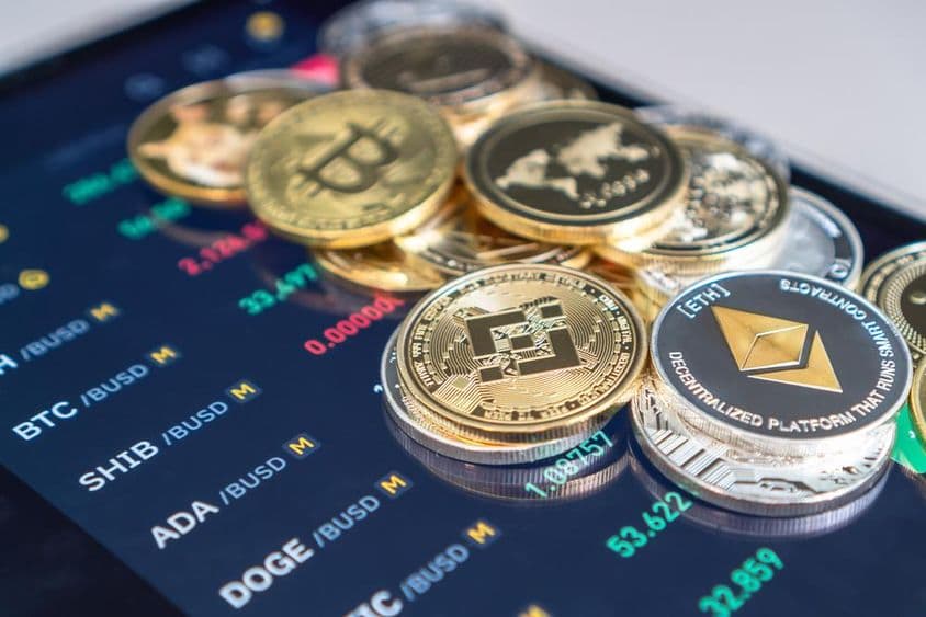 Monedas de Ethereum y Bitcoin colocadas sobre una pantalla de teléfono que muestra tasas de cambio de criptomonedas.