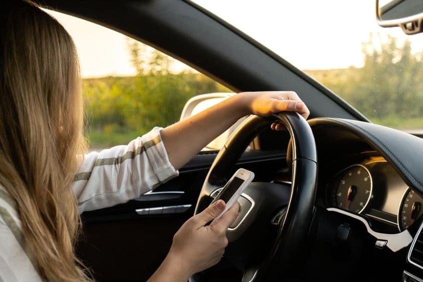 Una mujer usando un teléfono móvil mientras conduce, sosteniendo el volante con la otra mano.