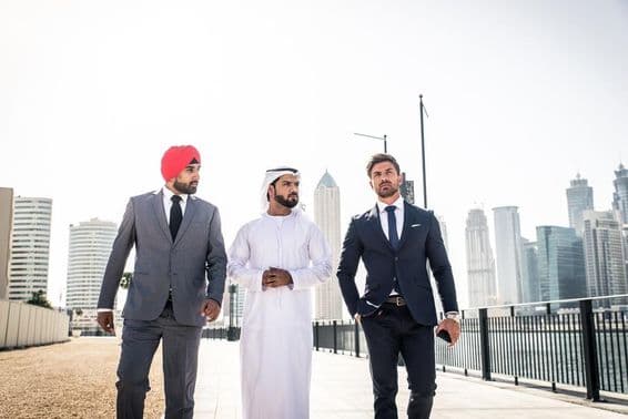 Un indio, un emiratí y un ciudadano europeo caminando por el canal, rascacielos detrás de ellos.