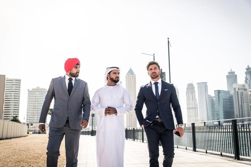 Un indio, un emiratí y un ciudadano europeo caminando por el canal, rascacielos detrás de ellos.