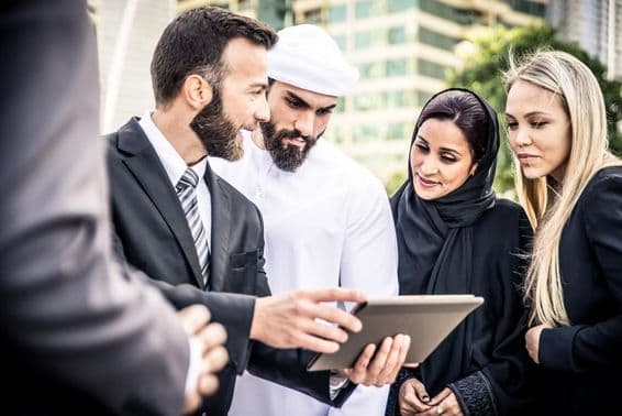 Un hombre europeo y un emiratí mirando una tableta, flanqueados por dos mujeres, una rubia y una emiratí, observando.