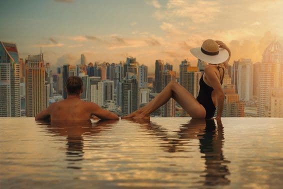 Pareja joven en una piscina con rascacielos al fondo.