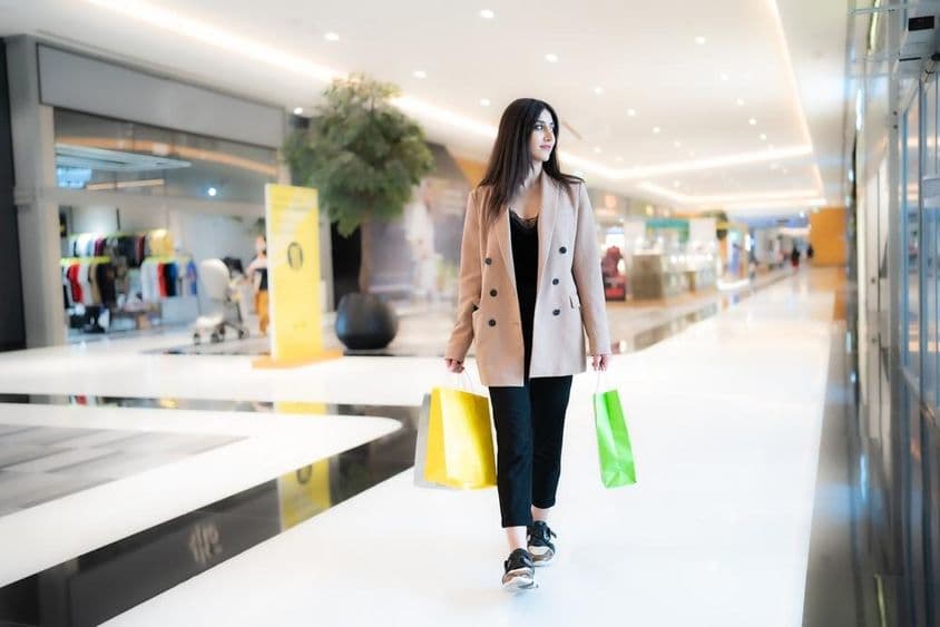Una mujer comprando en Dubai Mall, sosteniendo dos bolsas, con tiendas de fondo.