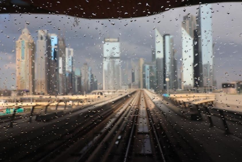 Lluvia vista a través de una ventana del metro de Dubái con rascacielos de fondo.
