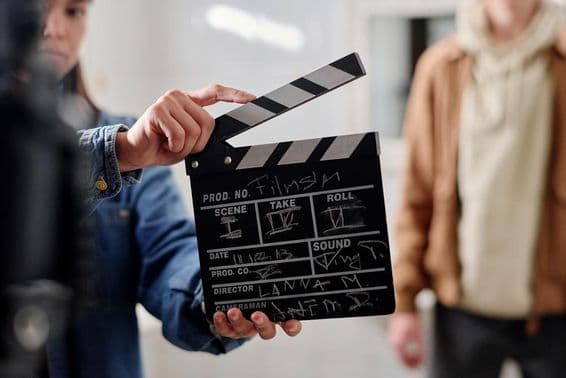 Claqueta de cine con escritura de tiza, dos personas al lado.