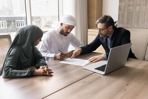 Una familia emiratí firmando un contrato frente a un corredor, con un cuaderno sobre la mesa.