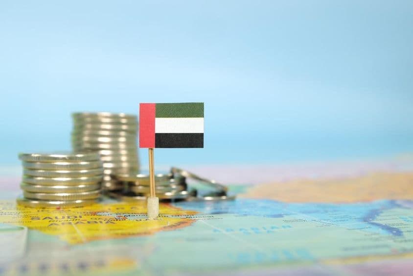 Una bandera de los EAU integrada en un mapa, con monedas apiladas al lado.