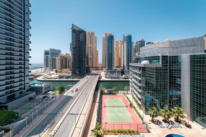 Una cancha de tenis en Dubai con rascacielos y una lancha en el agua.