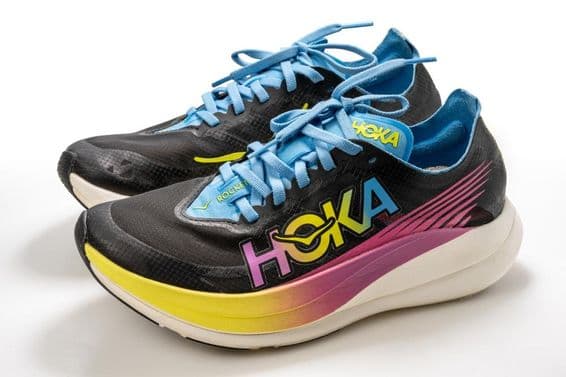 Una zapatilla deportiva Hoka con estampado colorido, predominantemente negra, con una suela blanca.