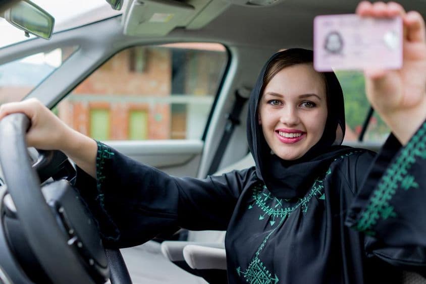 Una mujer en Dubái sostiene una licencia de conducir con una mano y el volante con la otra, sonriendo.